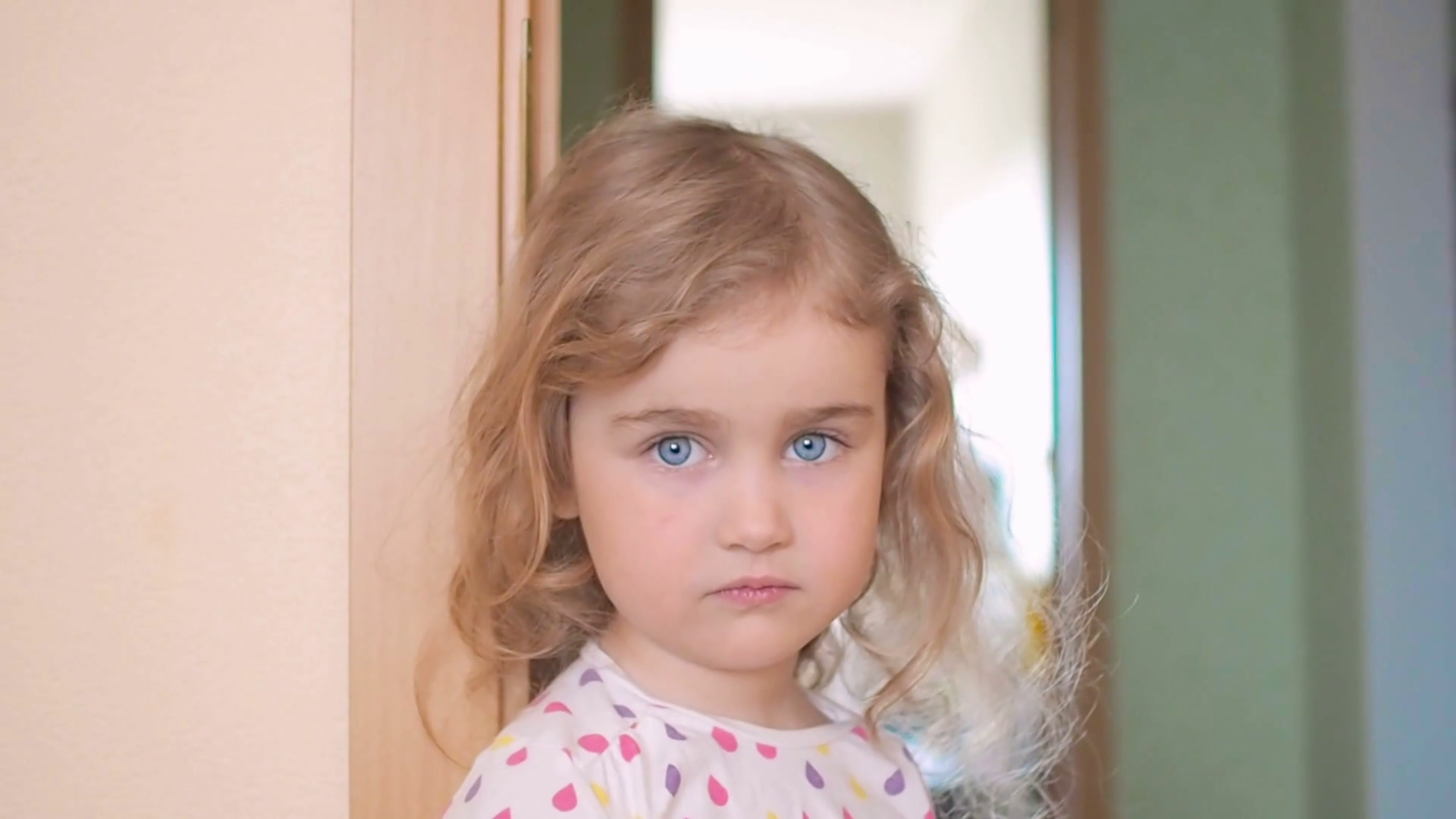 videoblocks-little-girl-is-blonde-with-blue-eyes-stands-near-the-wall-in-the-house-child-with-regret-looking-at-the-cameraportrait-of-a-sad-girl_hbzn27pal_thumbnail-full01